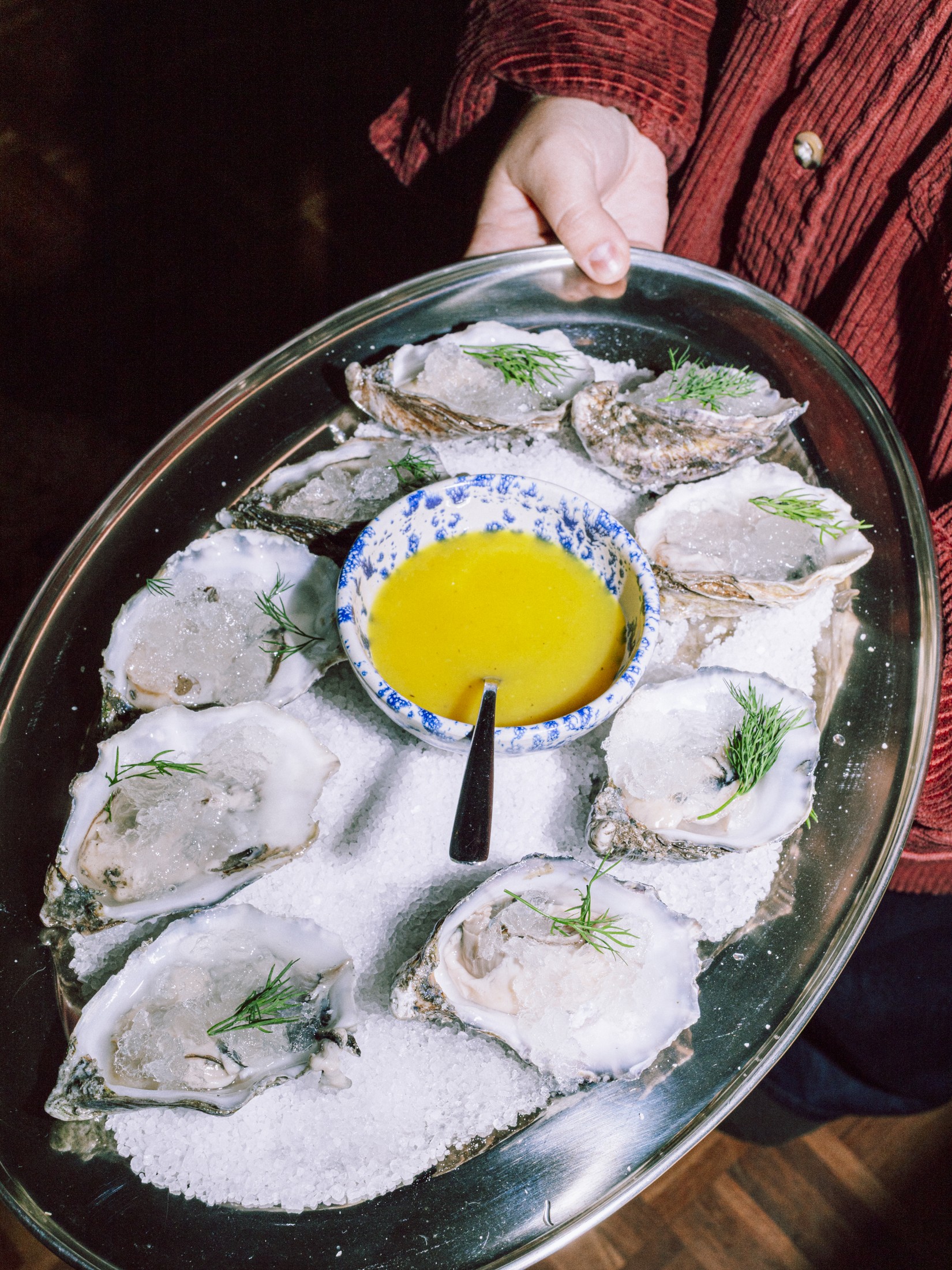 Overhead shot of fresh oysters on a platter with a pooled yellow sauce in the centre