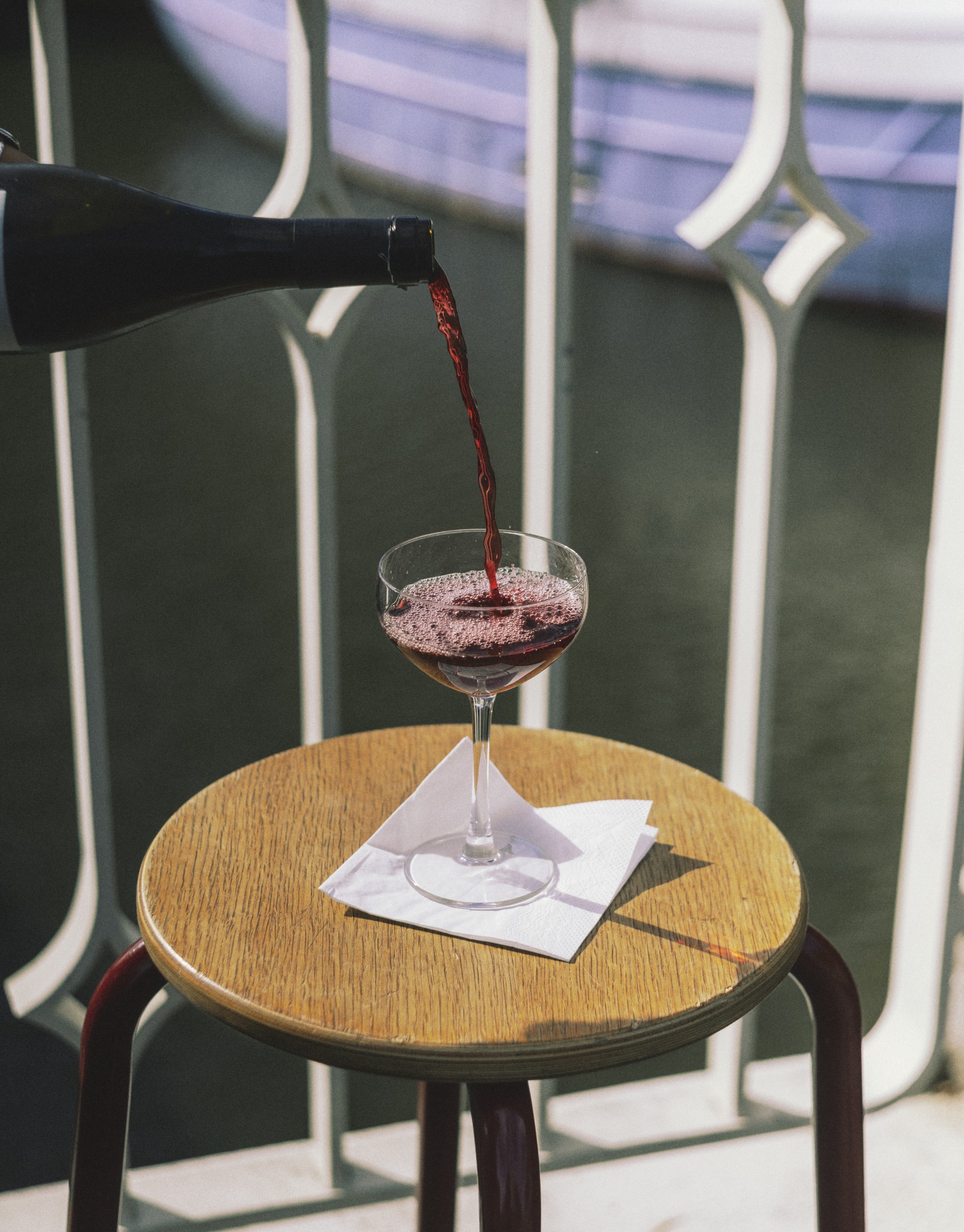 Red wine being poured into a glass on a small outdoor table