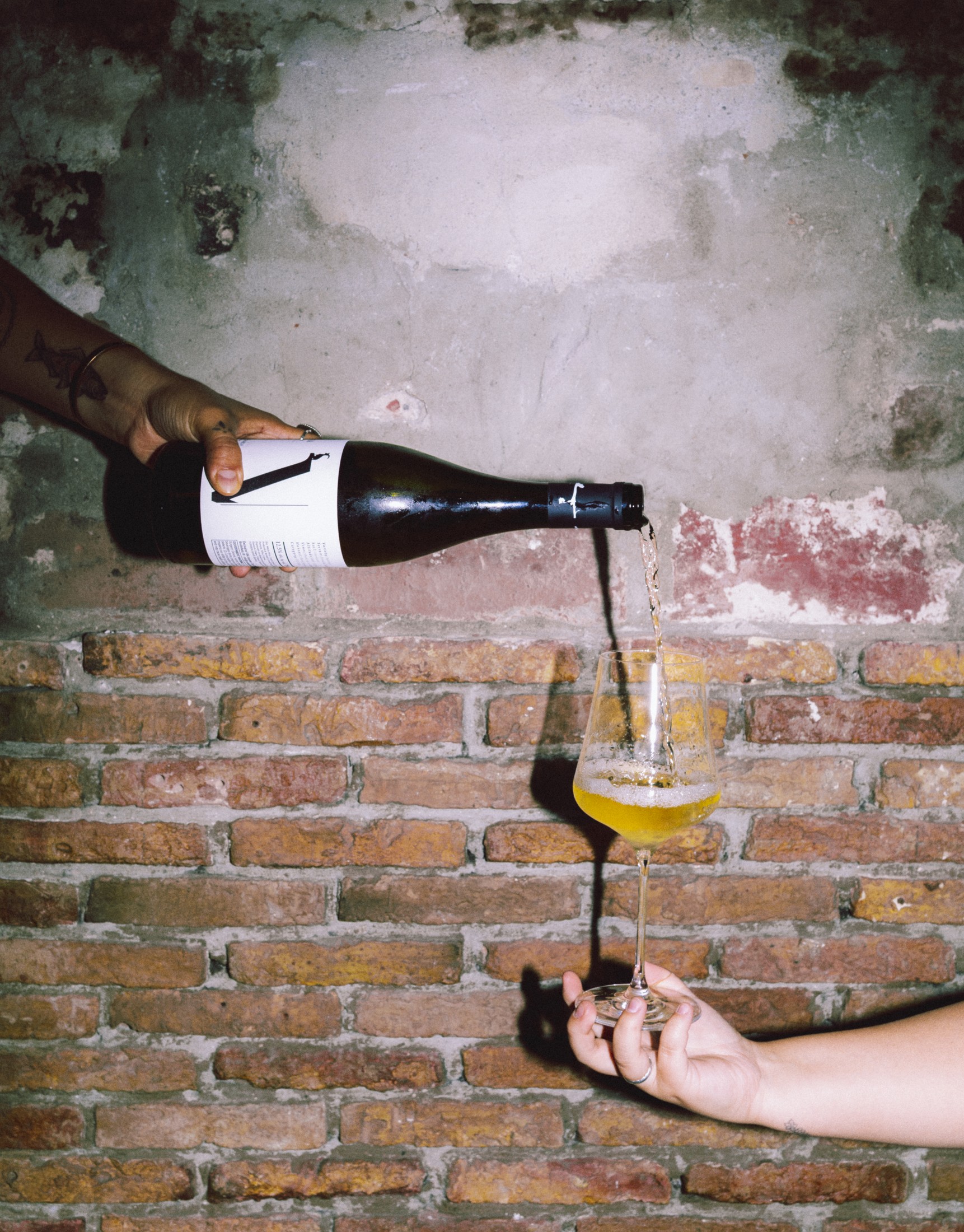Hand pouring sparkling wine over a brick ledge, caught mid-pour