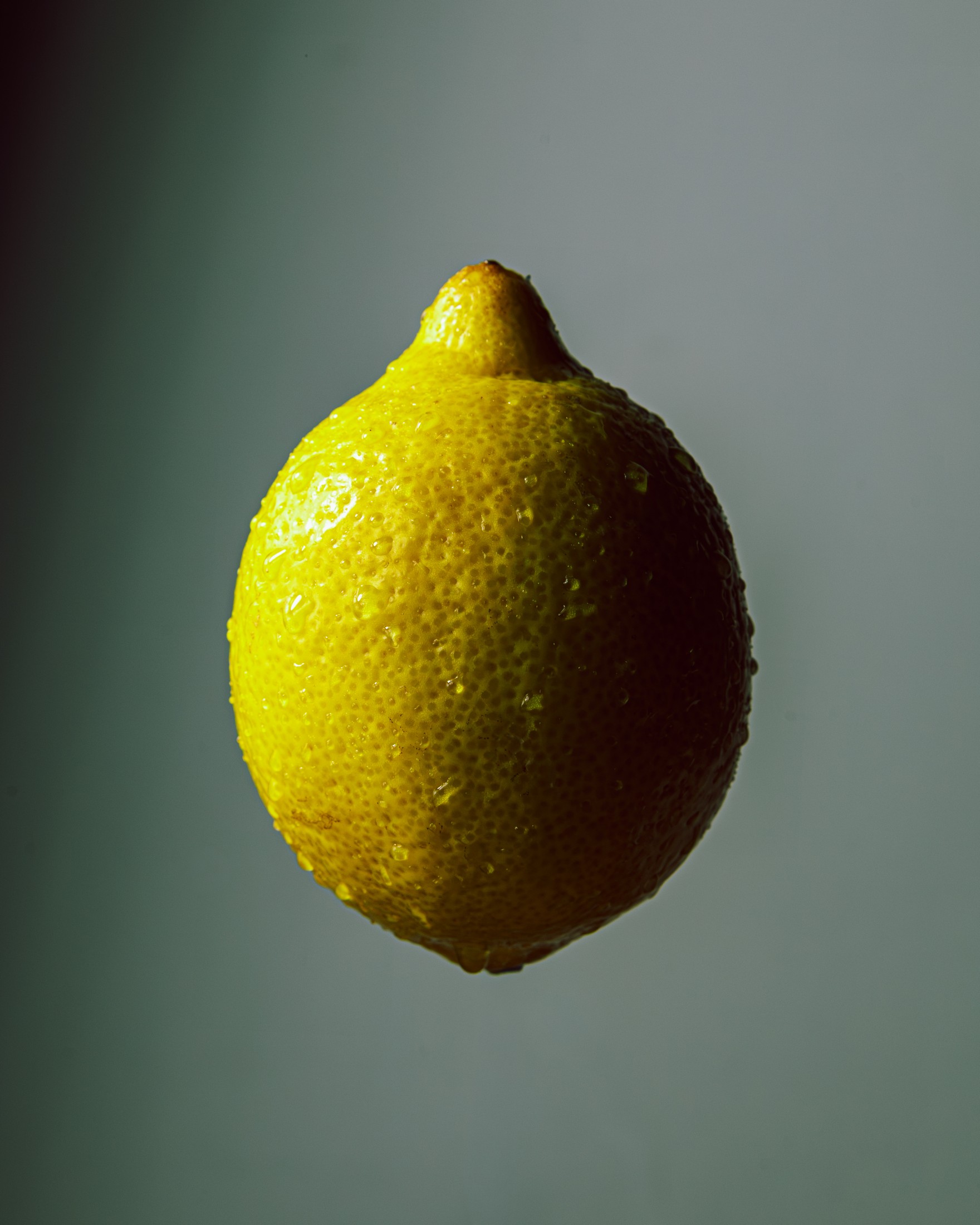 A single lemon lit dramatically against a teal background