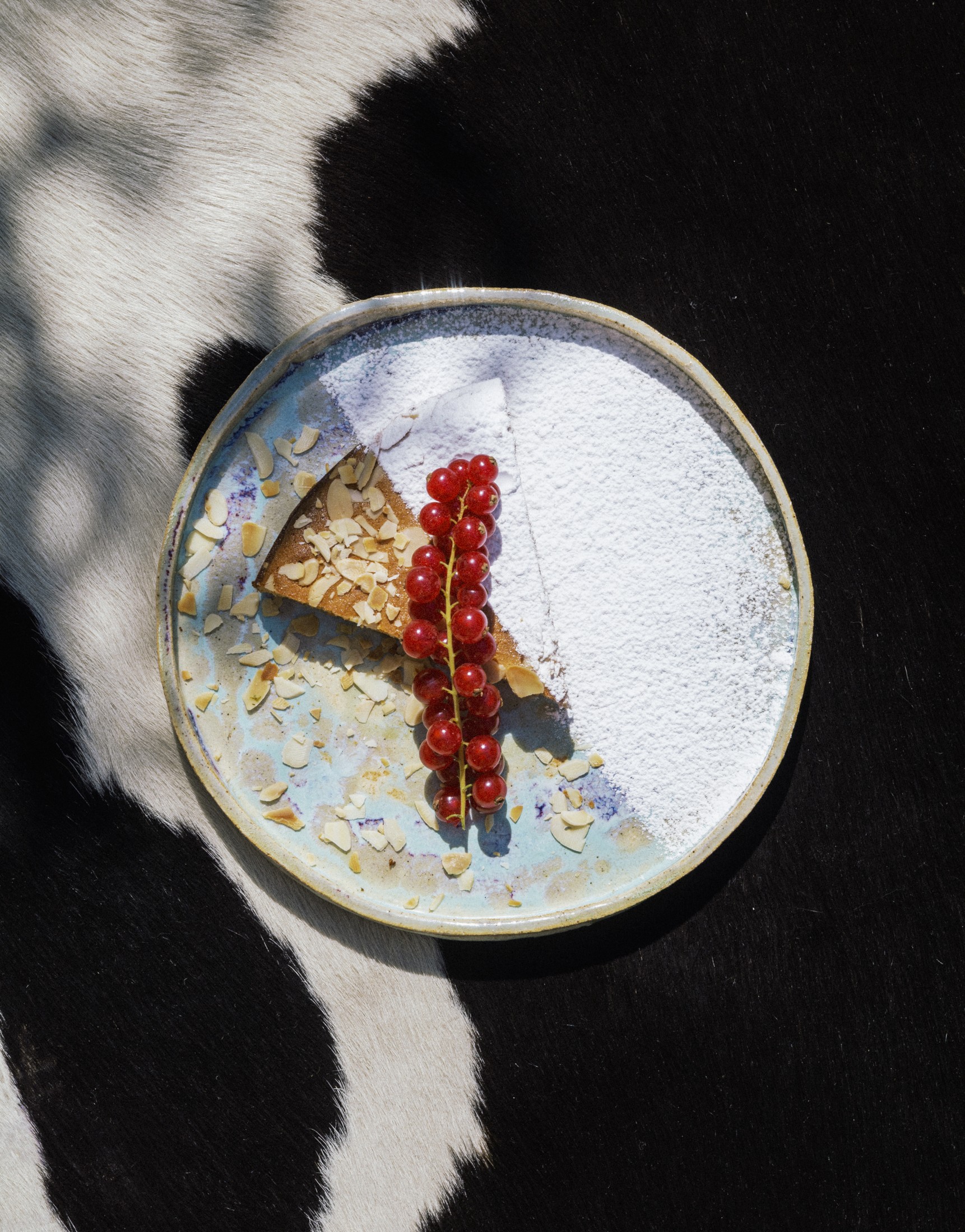 Slice of Spanish almond cake with powdered sugar and redcurrants on a blue ceramic plate