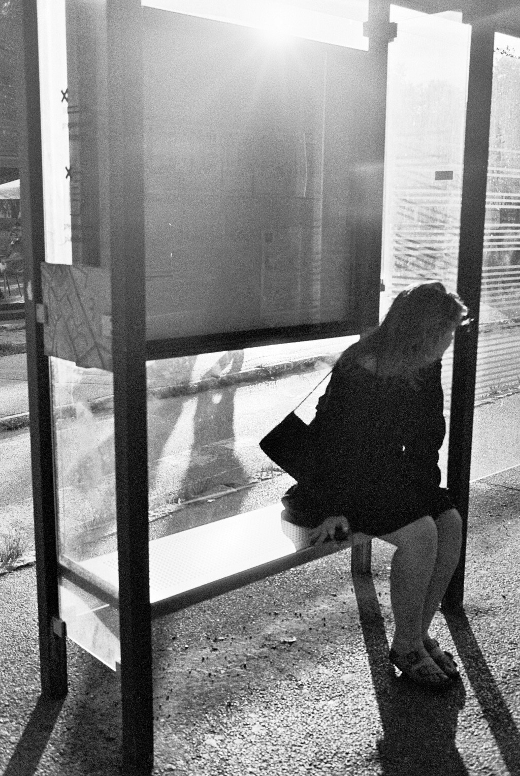 Silhouetted figure bending at a bus stop at night, grainy black-and-white street portrait