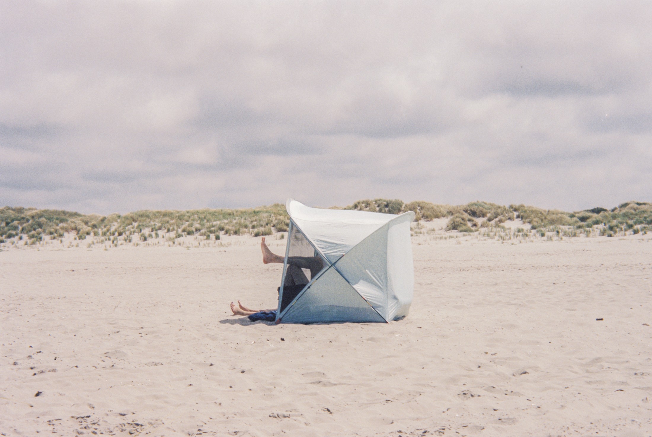 Beach scene with a windbreak tent and someone relaxing among the dunes