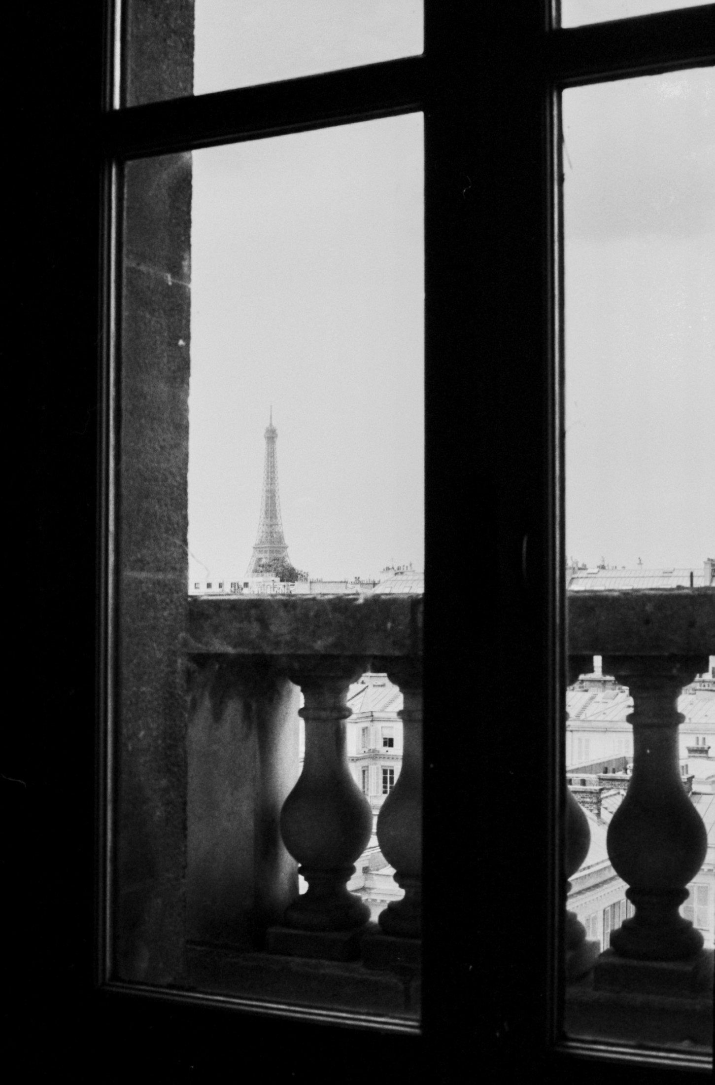Black-and-white view of the Eiffel Tower through an ornate balcony railing