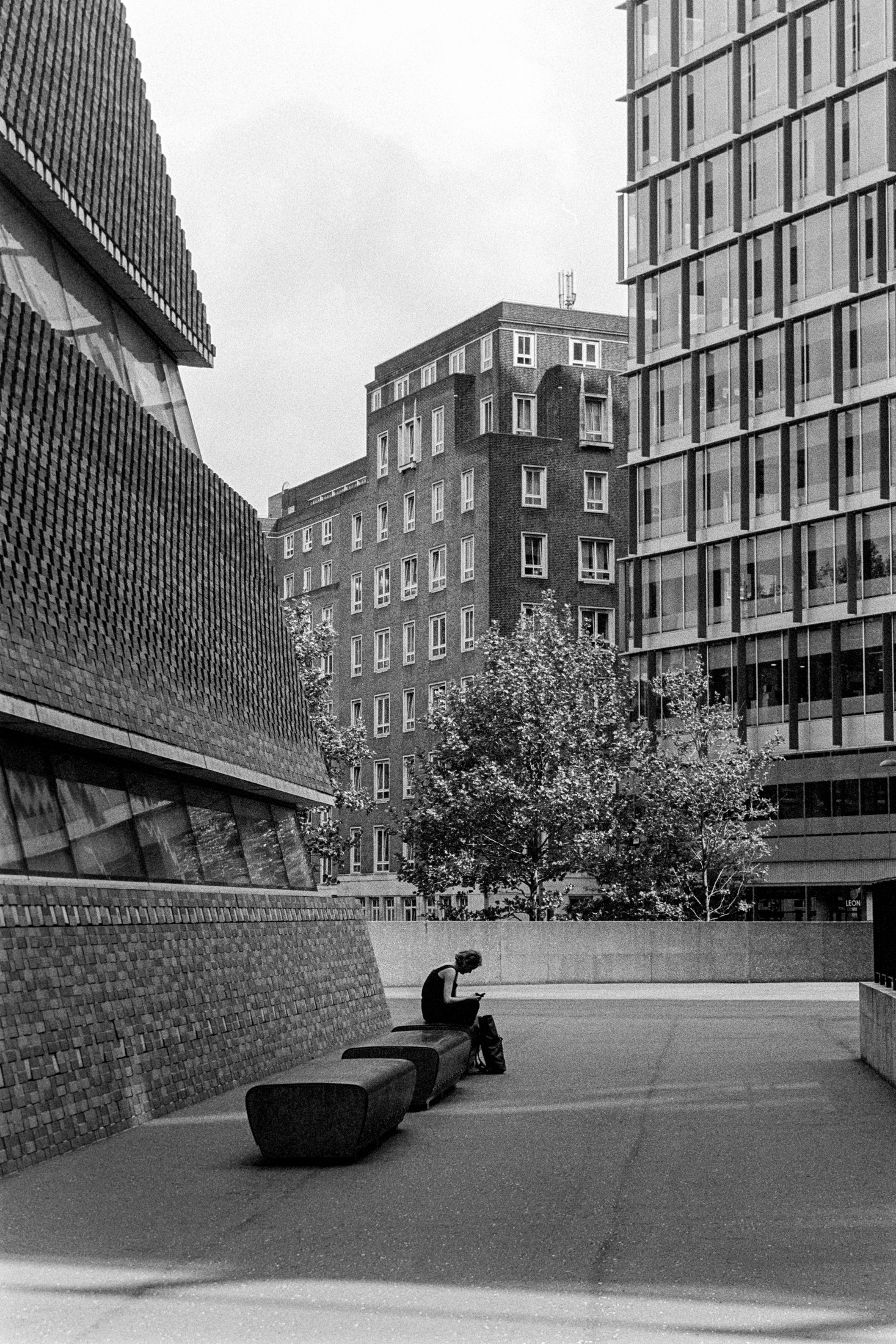 Black and white street scene with a figure seated on a bench between city buildings
